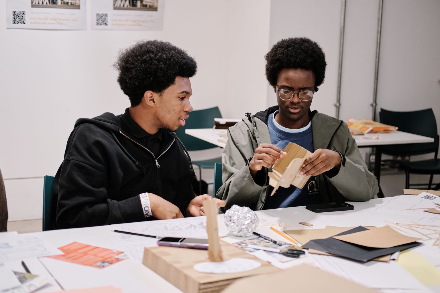 Two teenage students building a card model together